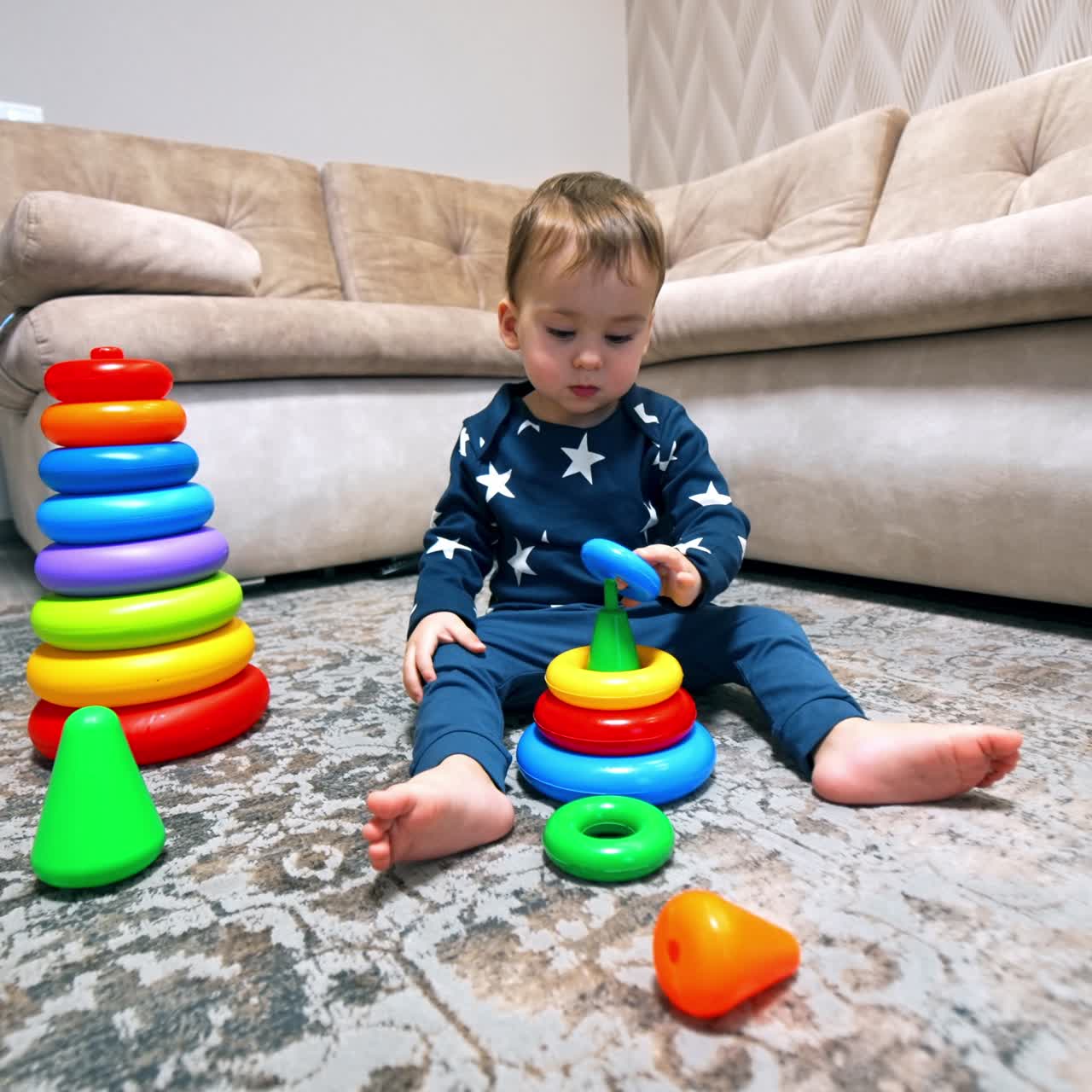 Cute lovely toddler building toy pyramid. Kid looks for the suitable ring around him on the floor