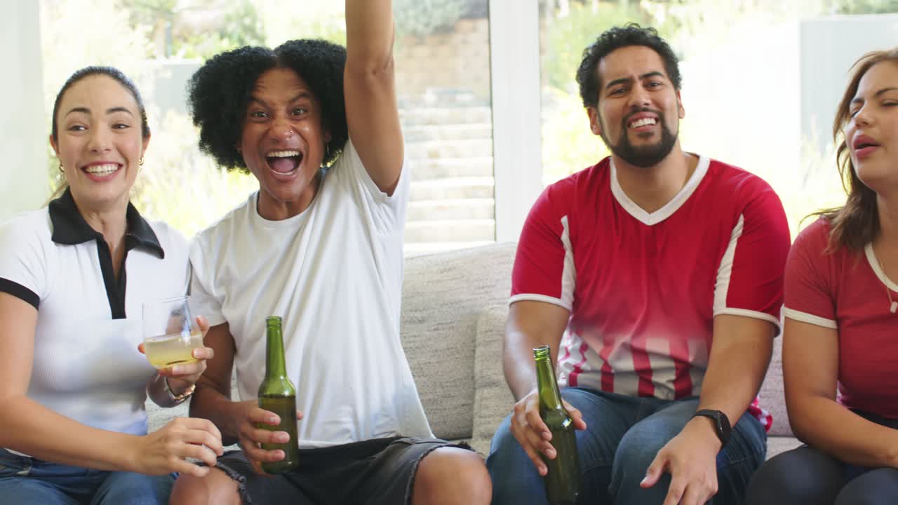 Diverse venner peker på en TV-kamp fra sofaen med en fotball, mens de holder drinker og jubler.