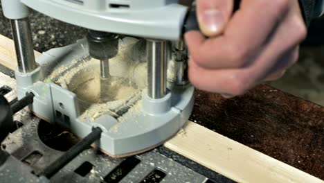 primer plano de la mano de un carpintero trabajando con un cortador eléctrico manual en un taller casero.