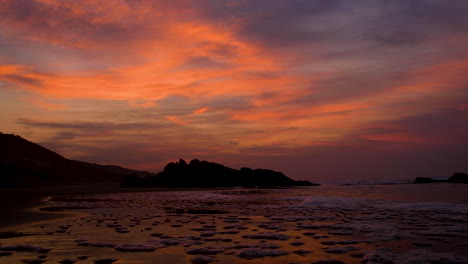 Tide gently pushing low foamy wave higher onto beach, spectacular golden sunrise