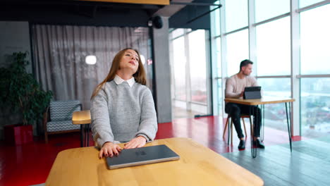 long-haired woman lying on her laptop tired from work. lady stretches her arms to the sides and opens her gadget to go back to work.