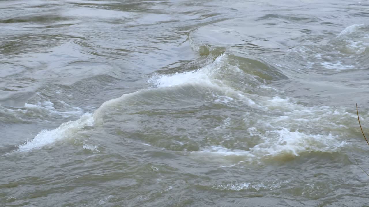 Waves with a strong current in a grey and brown river