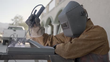 person in welding gear uses arc welder to fuse corner of angle iron- slow mo