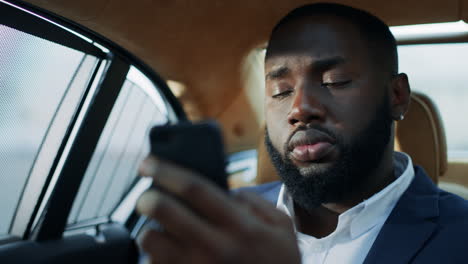 Retrato-De-Un-Hombre-De-Negocios-Africano-Enfocado-Escribiendo-Un-Teléfono-Móvil-En-El-Asiento-Trasero.