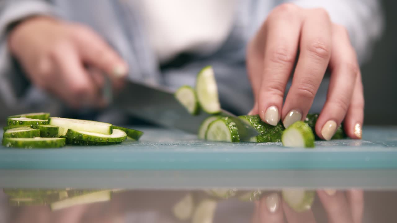 vista frontal de las manos de la mujer cortando pepino fresco en la tabla de corte en cámara lenta.