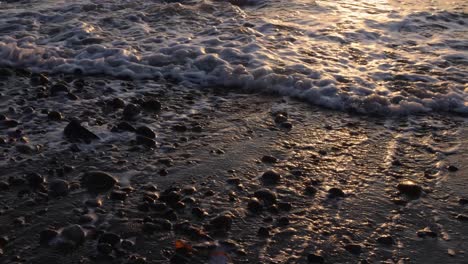 Primer-Plano-De-Un-Montón-De-Guijarros-Y-Rocas-En-La-Playa-Con-Olas-Entrando