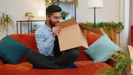 un cliente indio insatisfecho abre una caja de cartón y recibe auriculares inalámbricos dañados y rotos.