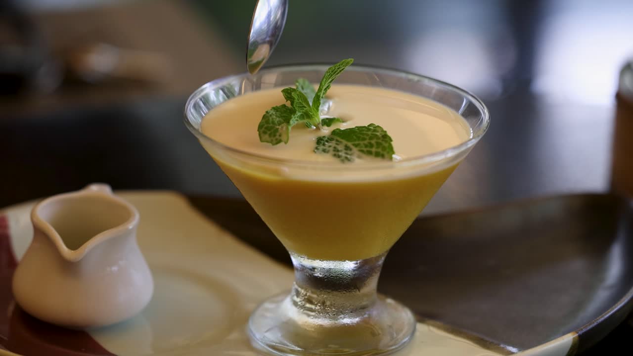 una cuchara sumergida en una cremosa crema de mango adornada con menta, destacando una deliciosa experiencia de postre