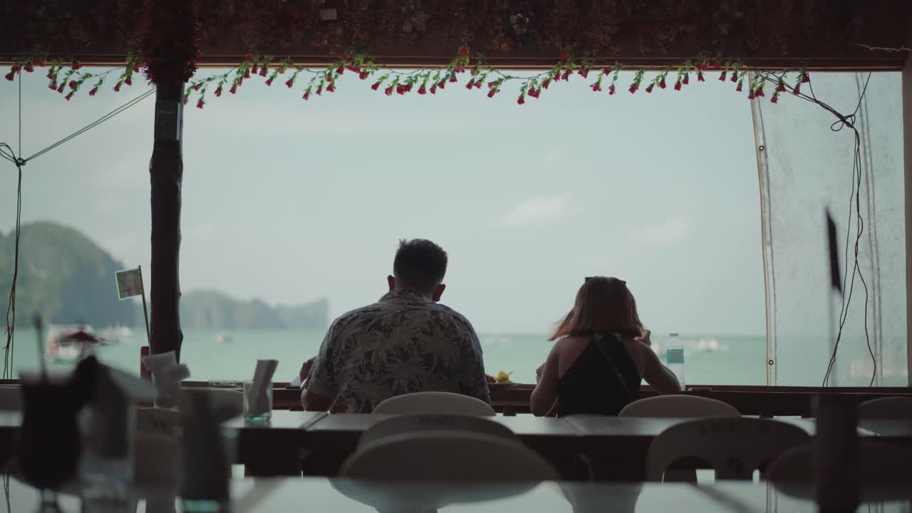 El Nido, Philippines - A Romantic Couple Eating Their Breakfast On An Open Restaurant While Feeling The Cold Breeze From The Ocean - Wide Shot
