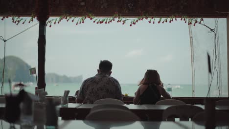 el nido, philippines - a romantic couple eating their breakfast on an open restaurant while feeling the cold breeze from the ocean - wide shot