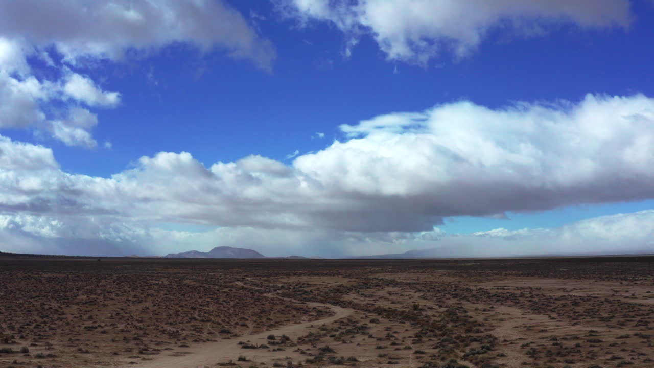 nubes cúmulos vigilan el paisaje accidentado del desierto de mojave - vista aérea deslizante