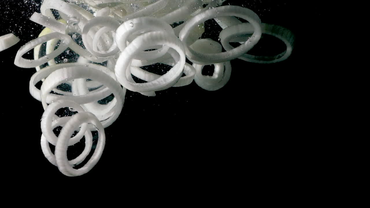 얇게 썬 양파를 검정색 배경에 물에 떨어뜨리고 측면 조명이 느린 동작