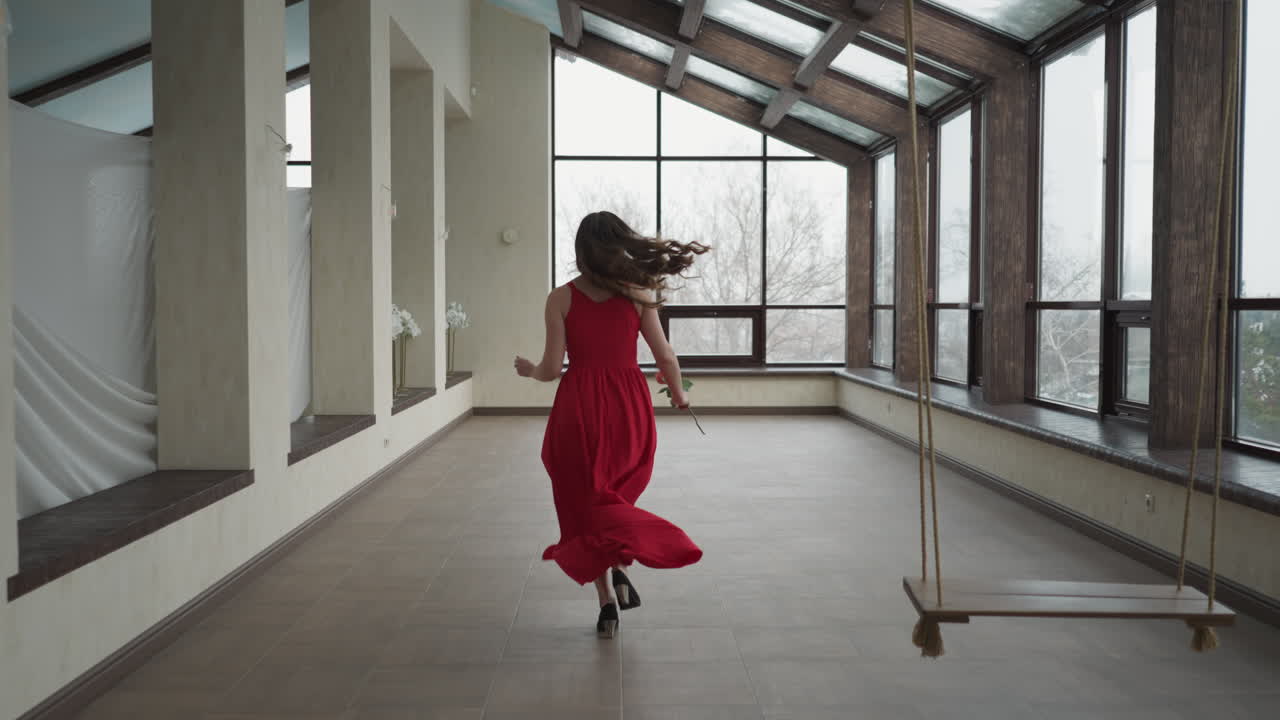 Model runs to window with rose in hand. Woman clutching flower in hand becomes chromatic embodiment of dynamic beauty. Vivid splash of colours in gallery