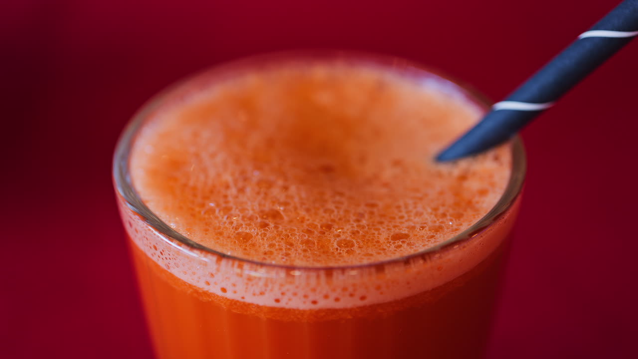 Close up of an orange and carrot juice in a glass with a black straw on a red table cloth