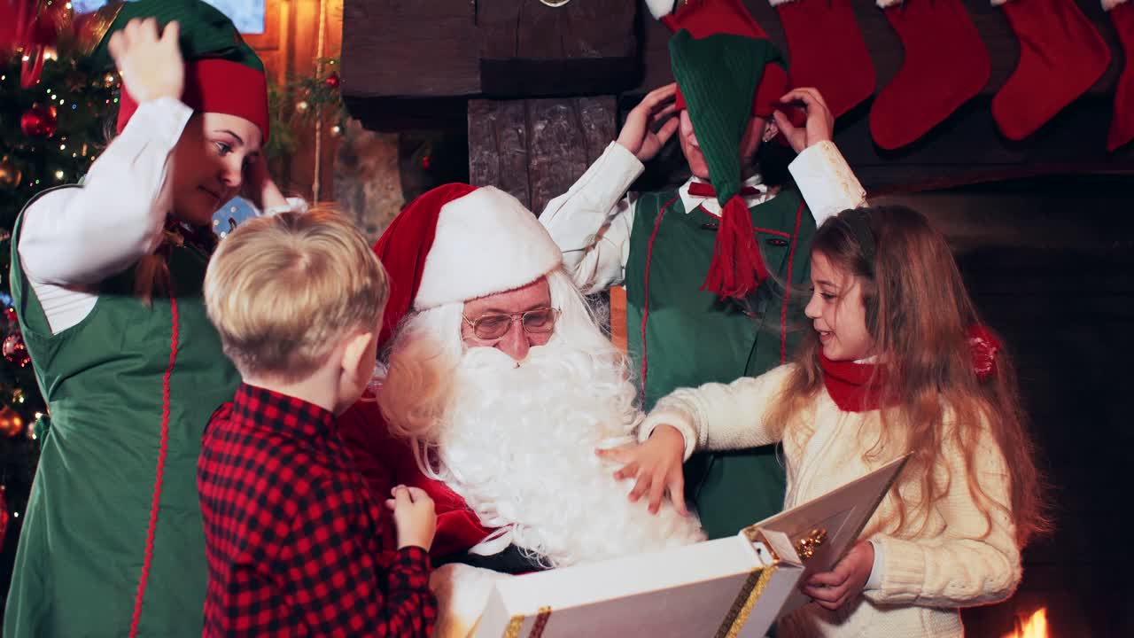 Children and elves play with Santa Claus near the fireplace with Christmas stockings