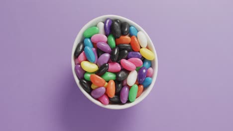 Video-of-close-up-of-multi-coloured-sweets-in-bowl-over-purple-background