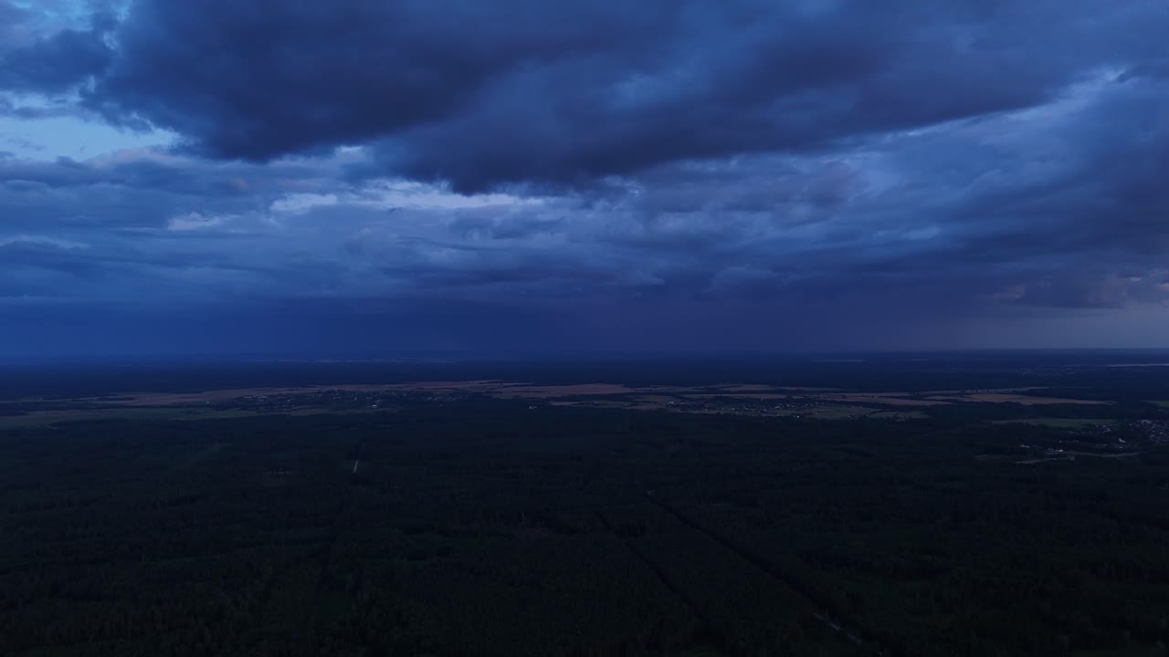 The sun sets, storm clouds fill the sky, creating a dramatic atmosphere over a rural landscape. Twilight enhances light and shadow contrast, painting the horizon, drone static footage