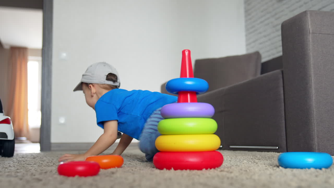 Caucasian kid in a cap sits near the toy pyramid. Smiling kid runs up to switch on the light. Low angle view.