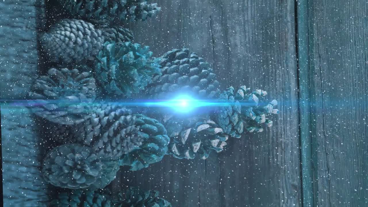 Animation of snowfall over illuminated lens flare against pinecones on wooden table
