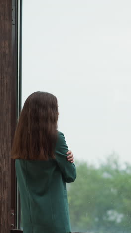 woman gazes at droplets cascading down glass. businesswoman finds moment of respite from chaos of corporate world on terrace. rain-drenched clouds