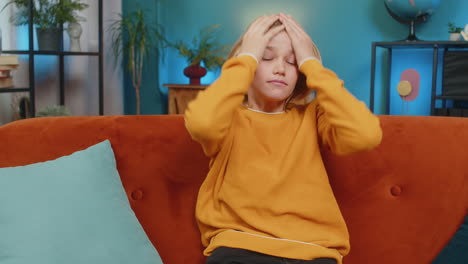 teenager boy holding head stressed expression thinking deeply after bad day sitting on sofa at home