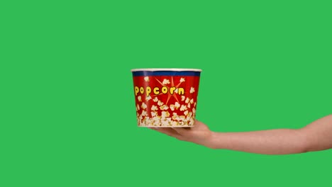 female hands giving a bucket of popcorn close up. woman points to the box and makes a thumbs up gesture. a container with a delicious snack on the background of a green screen chroma key. slow motion