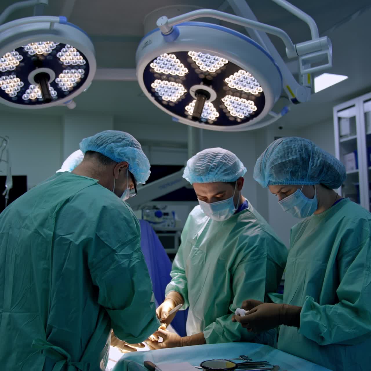 Three male surgeons carrying out the operation in modern clinics. Female nurse assisting the doctors preparing tools for them