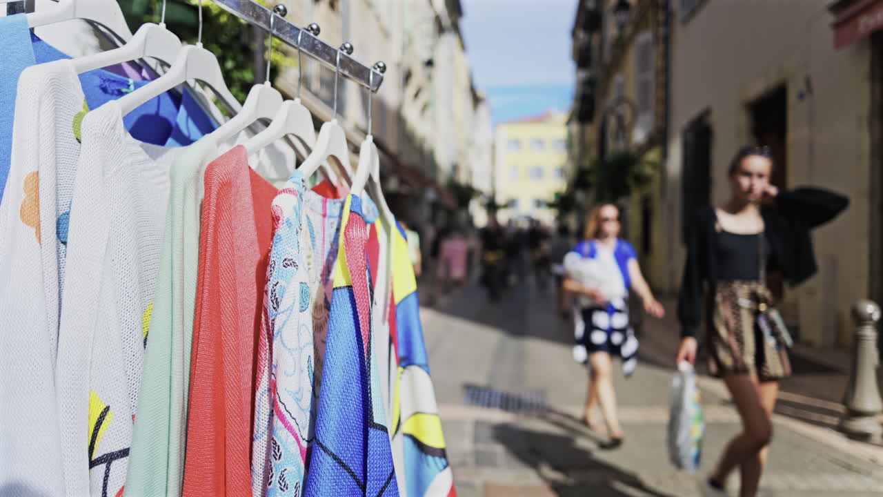 Close up of clothes for sale on a rack with a blurred view of people walking on the streets of Antibes, France
