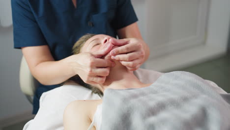 participant lying on massage bed face up as skin care expert cradles jawline gently with fingertip support under soft lighting for relaxation comfort and skin rejuvenation during facial therapy
