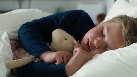 little caucasian girl sleeping in bed with teddy bear.