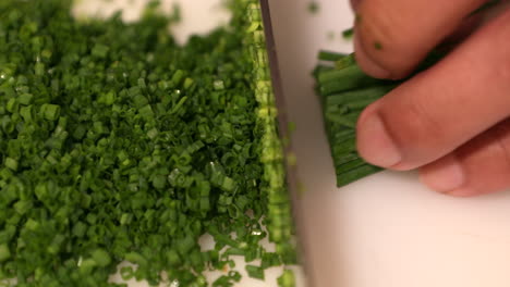 a skilled chef slicing thinly the fresh green onion chives on a chopping board in the kitchen