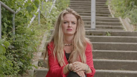 young blond woman sitting on park steps and looking seriously at camera