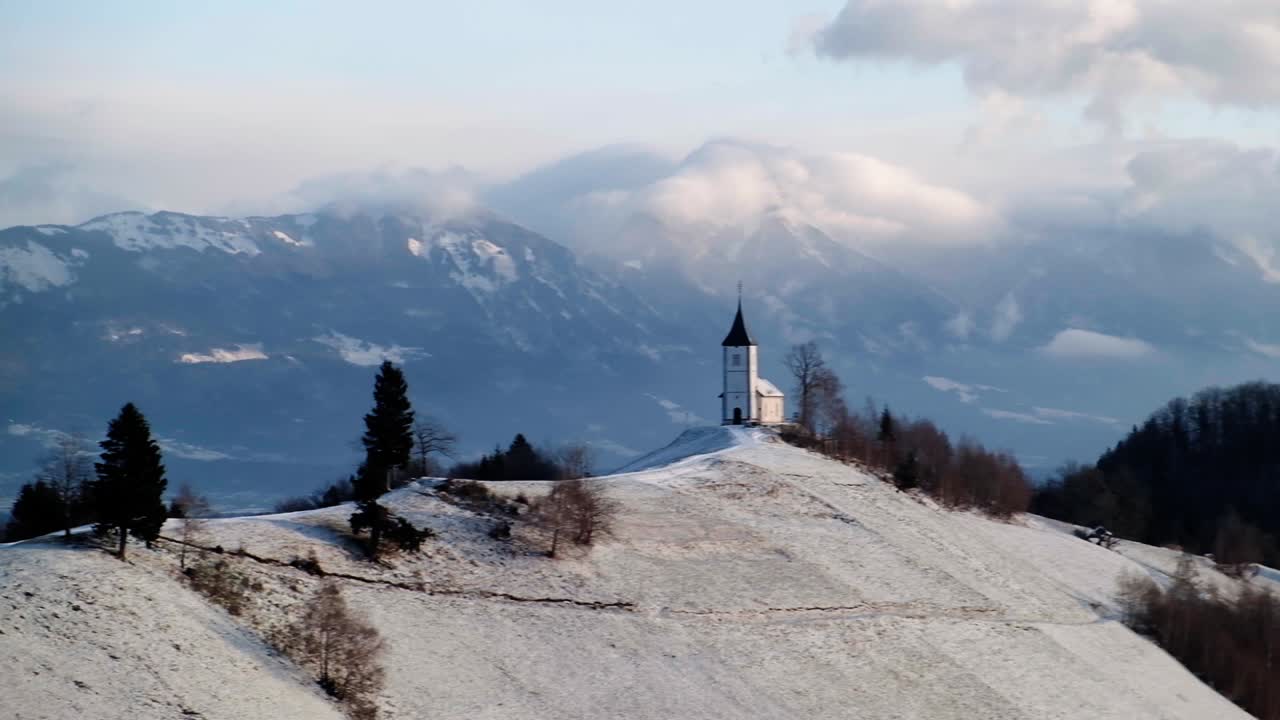 Pohled na kostel Jamnik v zimní krajině s barevným východem slunce v Kranji, Slovinsku.
