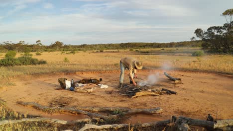 a bushman put wood on his campfire in the australian outback