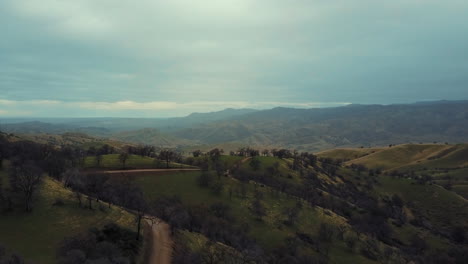 Aerial-dolly-zoom,-road-winding-in-green-foothill-mountains,-foggy-blue-morning