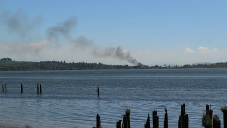 Humo-De-La-Práctica-De-Fuego-Para-El-Campamento-Rilea-En-Youngs-Bay-Oregon-Mirando-A-Través-De-Los-Pilones-De-Un-Antiguo-Muelle-Mientras-El-Humo-Se-Dispara-Hacia-La-Izquierda-Durante-Un-Minuto