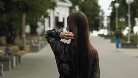 woman with long loose hair walks on city promenade back view