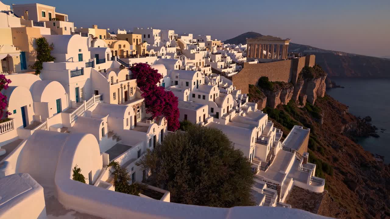 Aerial video captures a stunning sunset view of white buildings on a cliffside in Santorini, Greece