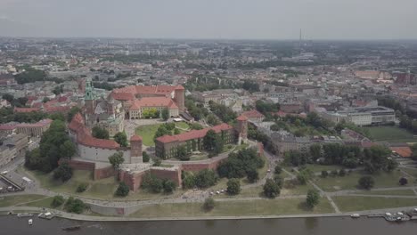 Polen,-Krakau-Drohnenaufnahme,-Die-Von-Der-Vorderseite-Des-Schlosses-Wawel-Mit-Wisla-Im-Vordergrund-Und-Gebäuden-Im-Hintergrund-Herauszoomt