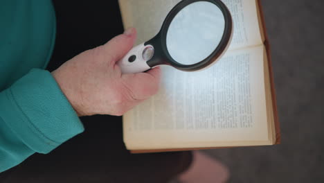 senior woman using magnifying glass to read book, close-up of hand holding magnifier over text, highlighting focus on reading, with natural light illuminating book and hands