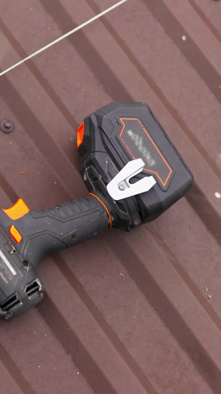 Un primo piano di un trapano nero e arancione con un pacco batteria appoggiato su una lamiera ondulata marrone.