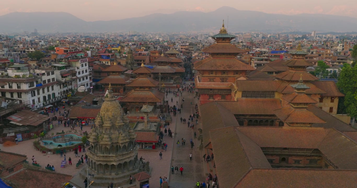 Dronekuva Patan Durbar -aukiosta, jossa näkyvät Krishna Mandir -temppeli, pagodatyyliset temppelit, perinteiset Newari-katot, iltakävijät ja Kathmandun laakson kaupunkimaisema sumuisten kukkuloiden taustalla auringonlaskun aikaan.