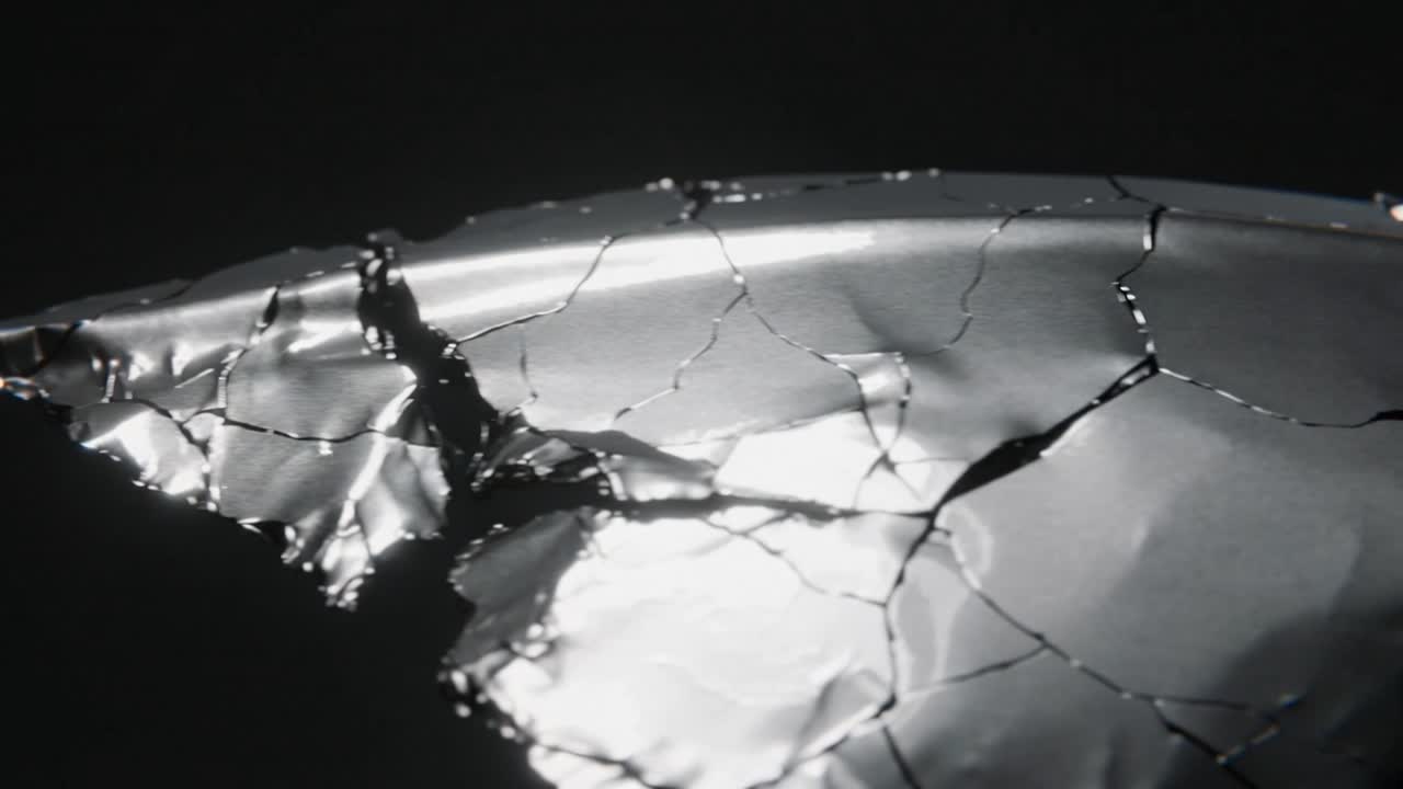 Shifting camera revealing metal foil cracks spreading to show texture in studio, with bright gleam