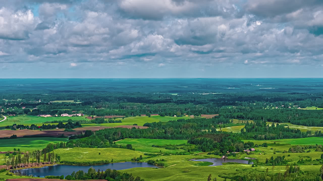 An aerial ballet of light and shadow unfolds in this captivating timelapse over Latvia's serene countryside as clouds sculpt verdant landscape of forests and fields beneath a vast, ever-changing sky