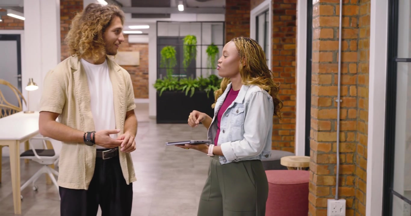 Diverse collega's lopen door kantoorgang, vrouw tikt op tablet en presenteert projectdetails