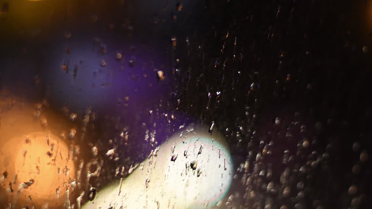 gotas borrosas de lluvia nocturna en una ventana sucia con luces bokeh en el fondo