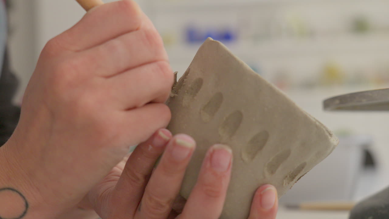 Masterfully etching intricate designs into soft clay with a specialized tool, showcasing artisan's delicate touch