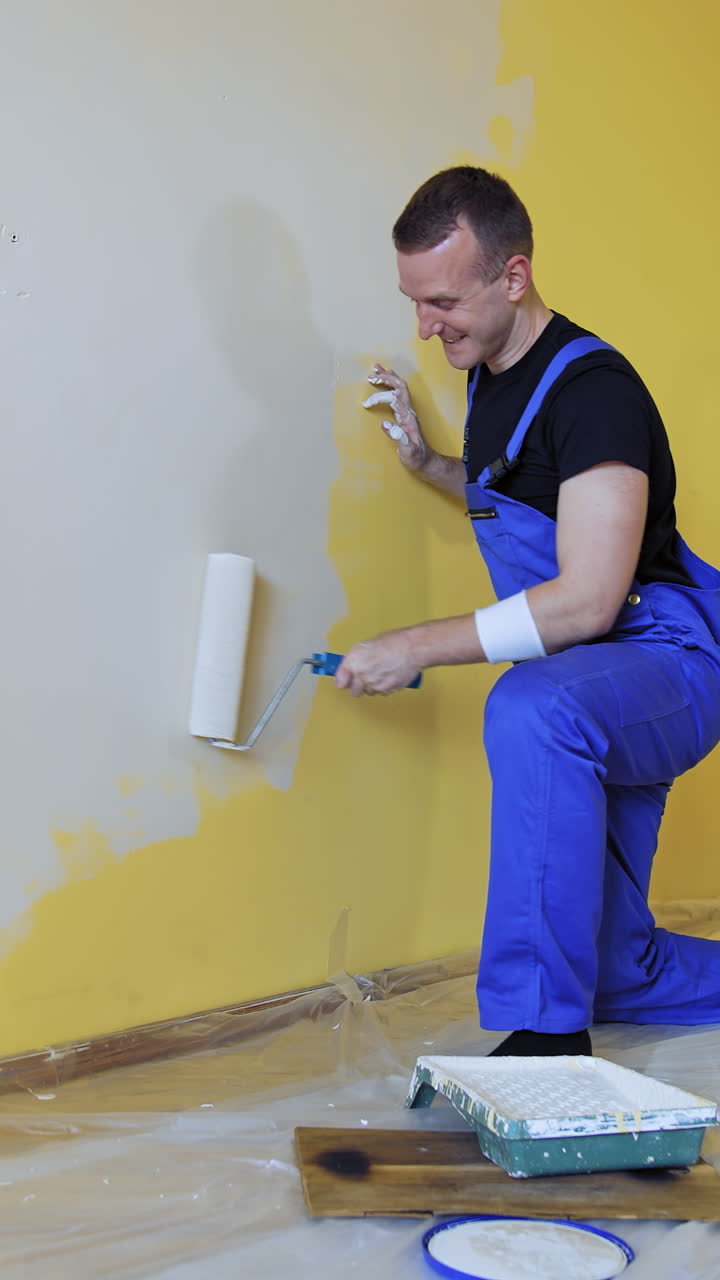 Happy male worker is painting wall. Professional young man with paint roller having fun in the apartment. Room painting job. Renovation home concept. Vertical video