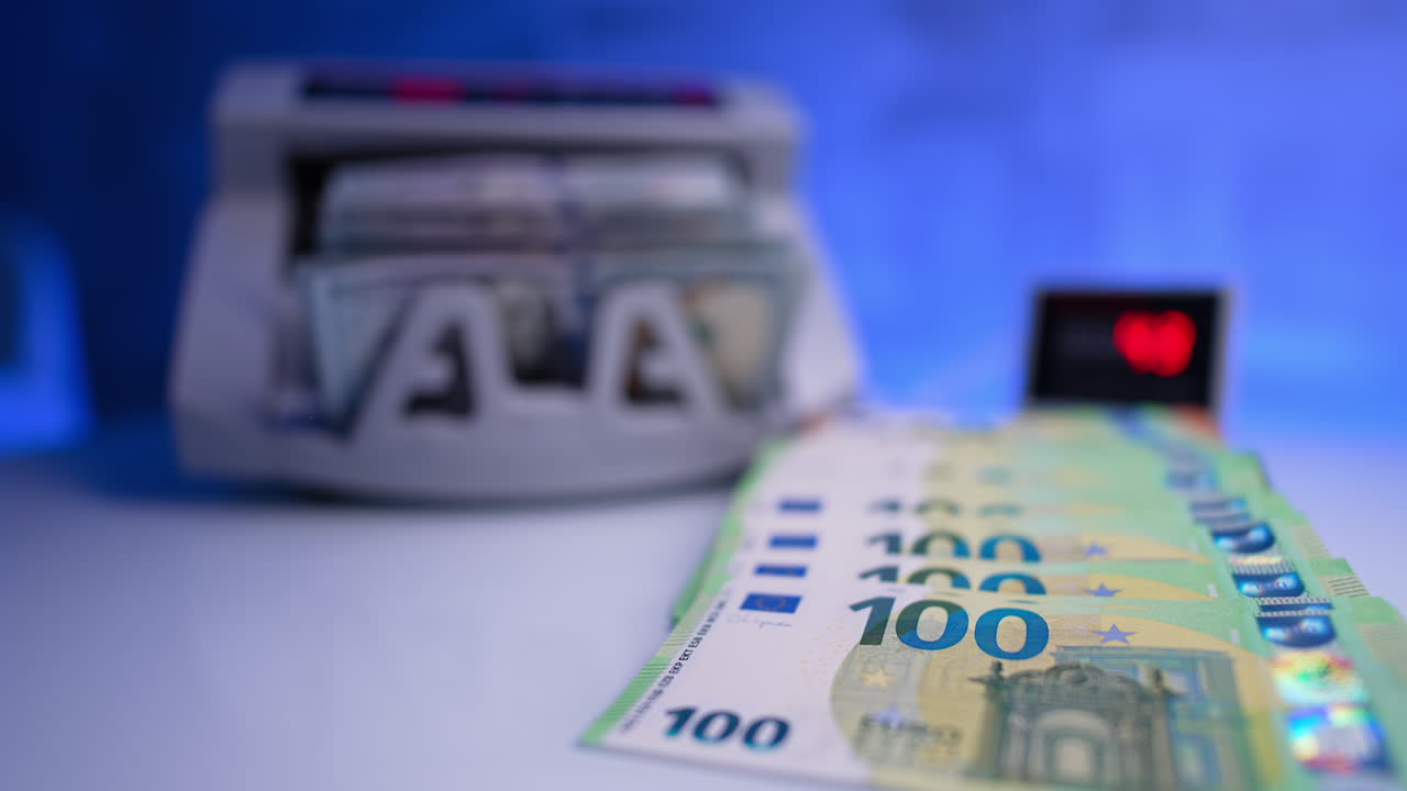 One hundred euro bills paced on the desk. Cash counting machine works at blurred backdrop. One hundred dollar bills are taken from device and placed near euro money. Close up.