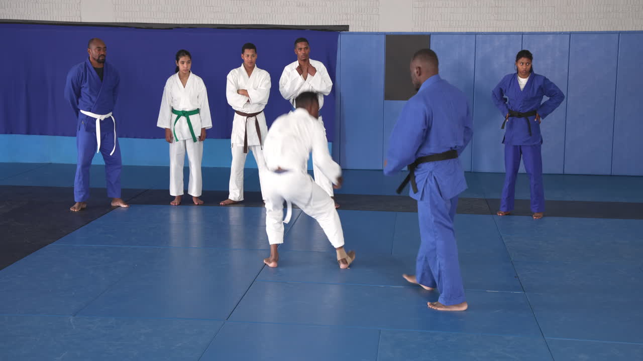 Practicing judo techniques, two men sparring on mat with classmates watching